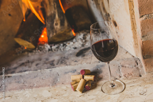 Taça de vinho tinto em lareira no inverno com rolhas e pinhas photo