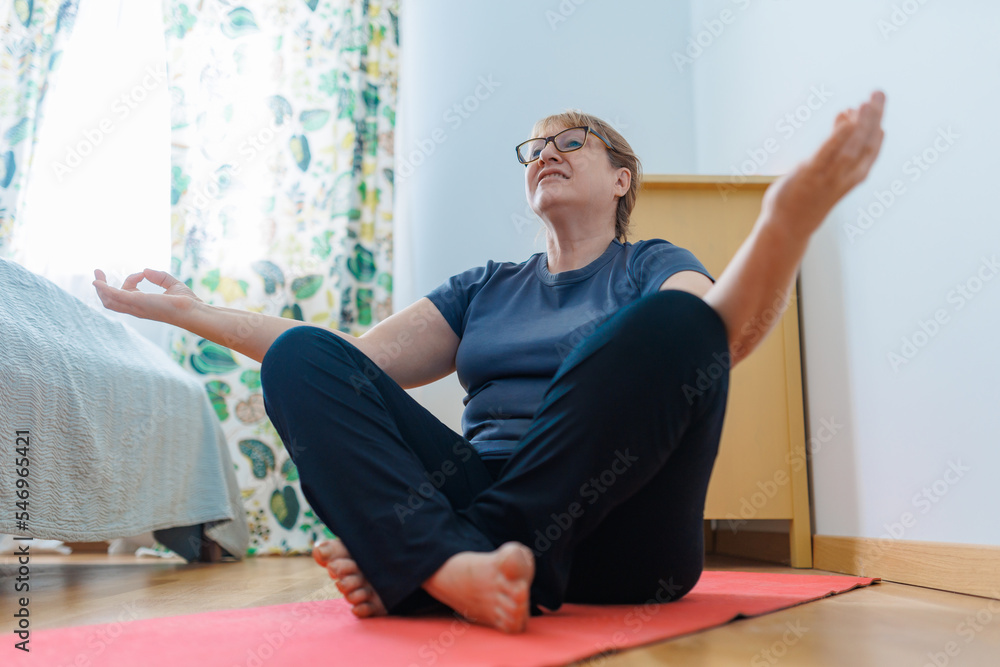 Fototapeta premium Active senior woman doing abs exercises on yoga mat at home and smiling at camera. Sporty mature lady working out in living room interior. Strength training concept