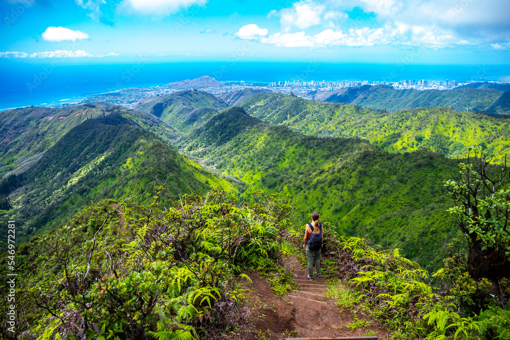 Fototapeta premium hiker girl enjoys the panorama of oahu island and honolulu in hawaii islands while climbing wiliwilinui ridge trail; hiking on green mountains in hawaii, holidays in hawaii