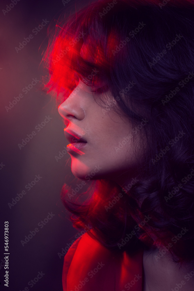 Closeup portrait of young woman with makeup and hairstyle, wear red suit, with closed eyes, red neon studio light.