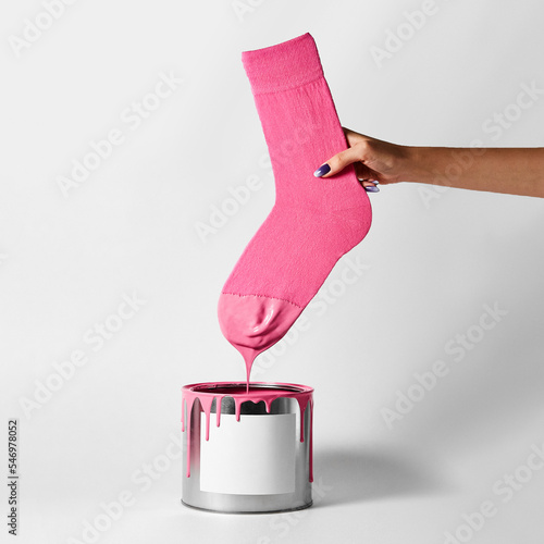 A female hand dips her pink sock into a can of paint photo