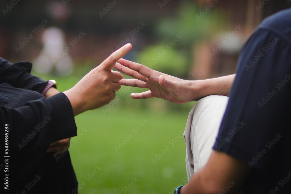 Couple in love having fun playing a hands game called Rock, Paper or Scissors game in a park.