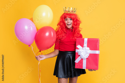 happy kid in crown with present box and party balloon on yellow background. wow
