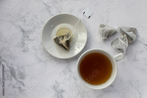 Cup of tea with tea bag on table. Green herbal tea in mug on white marble background. Top view. Traditional teatime. Teabag in cup 