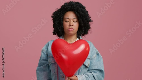 Black woman pops red balloon in shape of heart. Deeply upset beautiful African American woman feeling betrayed I will never forgive you, the love and relationships is over. Relations break off concept