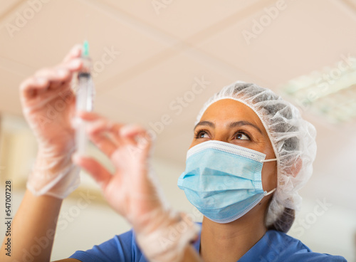 Female nurse in mask holding syringe for injection in hospital photo