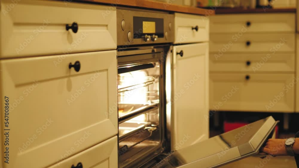 Close up of woman hand opening a modern cooking oven, kitchen utensils. Concept. Details of cooking process, putting a baking dish inside the oven. Close up of woman hand opening a modern cooking oven, kitchen utensils. Concept. Details of cooking process, putting a baking dish inside the oven.