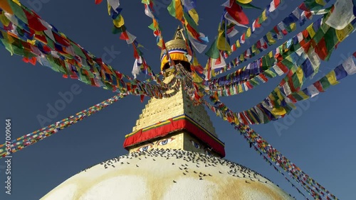 Boudhanath stupa in Kathmandu, Nepal. Camera moves between Buddhist flags swaying in the wind, pigeons sit on the dome of Boudhanath Pagoda. UHD, 4K gimbal shot, slow motion photo