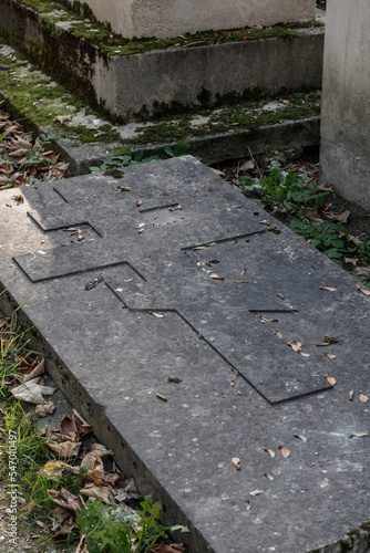 Anonymous gravestone engraved with the Russian cross in the Montmartre cemetery. The grave is mage of dirty grey stone.