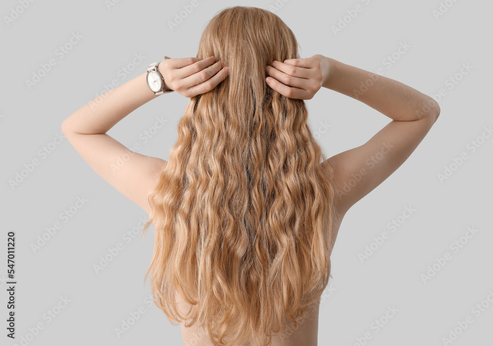 Young blonde woman touching curly hair on light background Young blonde woman touching curly hair on light background