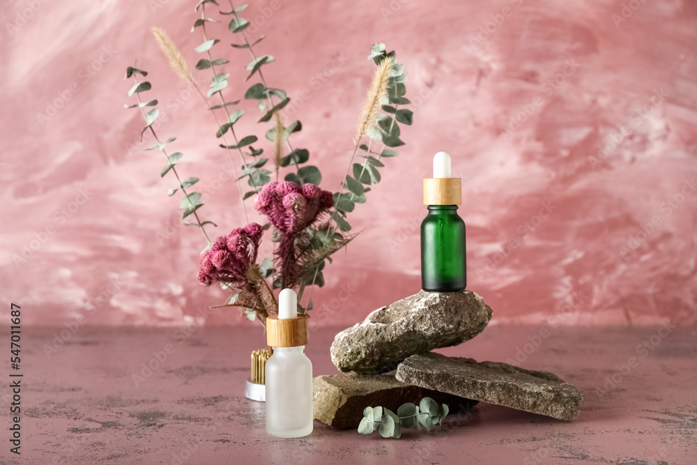 Cosmetic dropper bottles with rocks and ikebana on pink background Cosmetic dropper bottles with rocks and ikebana on pink background