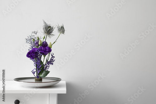 Bowl with beautiful ikebana on table near light wall photo