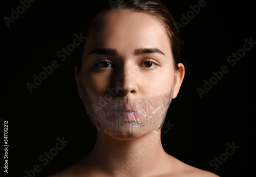 Billede på lærred Young woman with taped mouth on dark background
