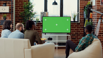 Multiethnic group of people enjoying tv show on greenscreen, watching movie with isolated mockup copyspace background. Looking at blank chroma key template to watch film at gathering.