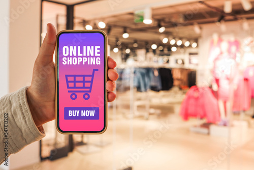 Online shopping. Phone in hand with the application of the site buy online against the background of a clothing store