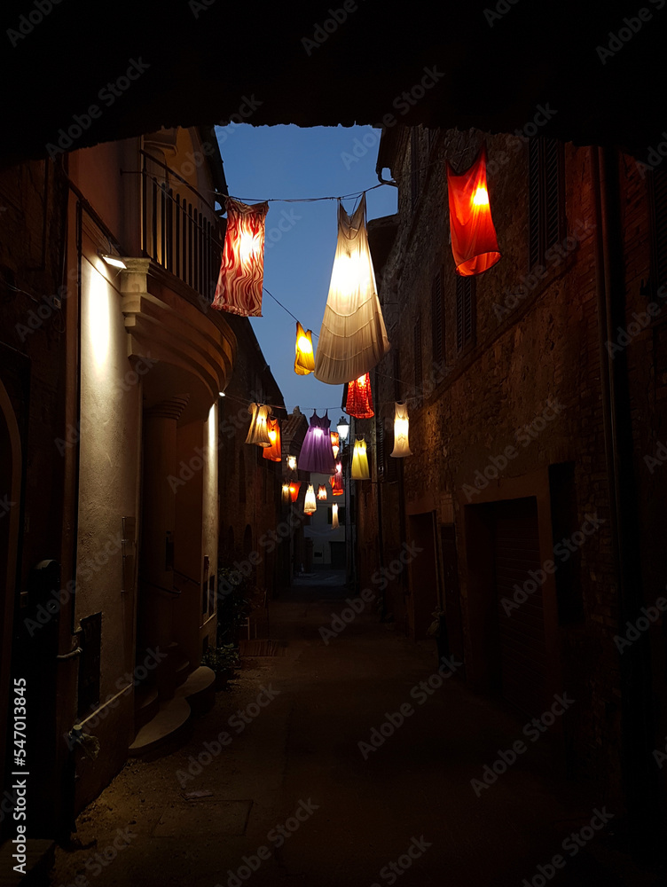 Interesting street lighting made of colorful dresses and nightgowns in a small town in Tuscany on a warm summer evening, Tuscany, Italy.