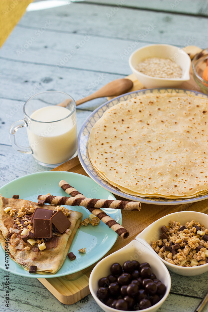 Crepes with chocolate on cutting board with ingredients. Rustic wooden background Crepes with chocolate on cutting board with ingredients. Rustic wooden background