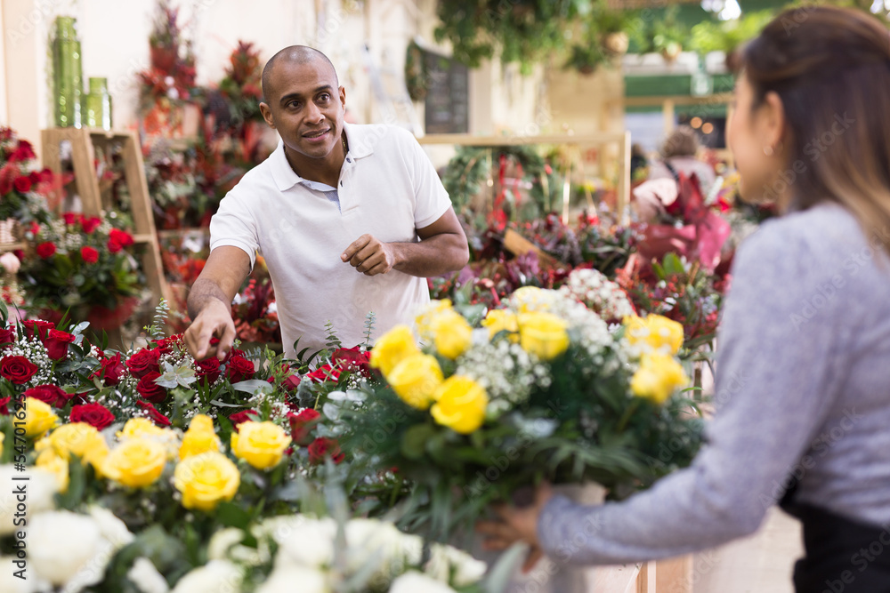 Woman owner of flower shop advising male customer before purchase of flowers
