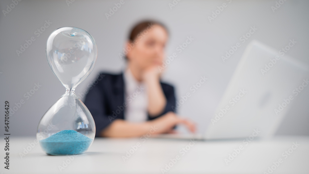 Business woman keeps track of time on an hourglass while working. Business woman keeps track of time on an hourglass while working.
