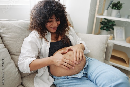 Pregnant woman smile and happiness lies on the couch freedom and strokes her belly with a baby in the last month of pregnancy, mother's day lifestyle