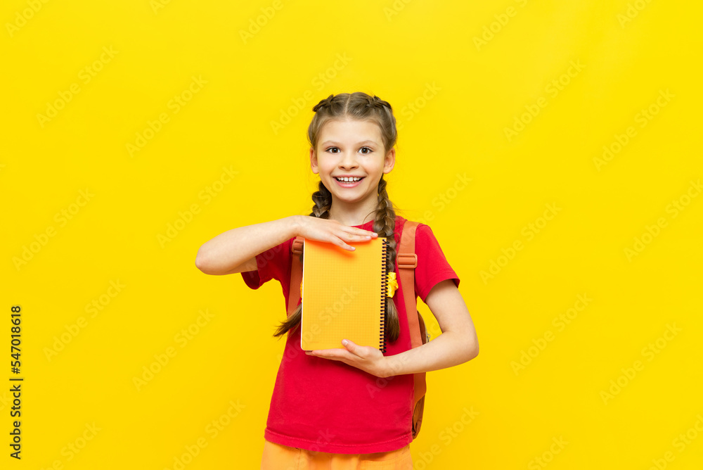 A little girl holds school notebooks in her hands. the child is preparing for school on a yellow isolated background. A little girl holds school notebooks in her hands. the child is preparing for school on a yellow isolated background.