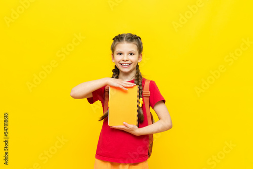 A little girl holds school notebooks in her hands. the child is preparing for school on a yellow isolated background.