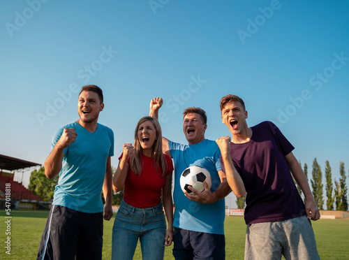 Group of people on soccer field with soccer ball cheering 