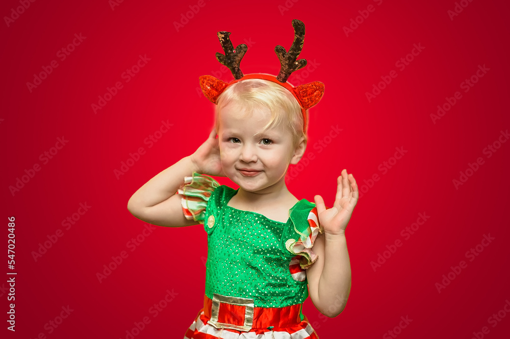 A funny little girl with Klaus deer roses on a red background. Christmas Day. New Year's photophone. A funny little girl with Klaus deer roses on a red background. Christmas Day. New Year's photophone.