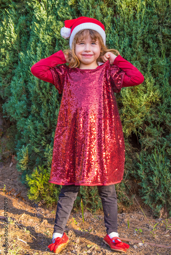 Beautiful little blonde girl posing in Christmas clothes and pine trees background