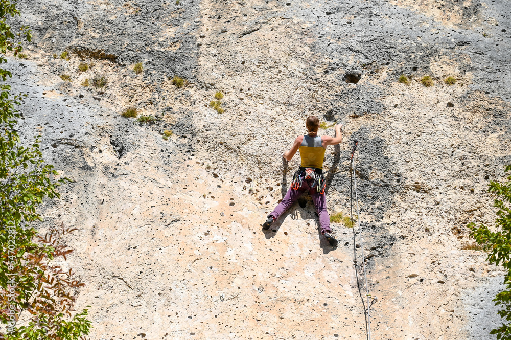 Woman climbing on rock. Climber climbs vertical and overhanging rock wall on mountain. Female climbs on rocky cliffs with ropes. 