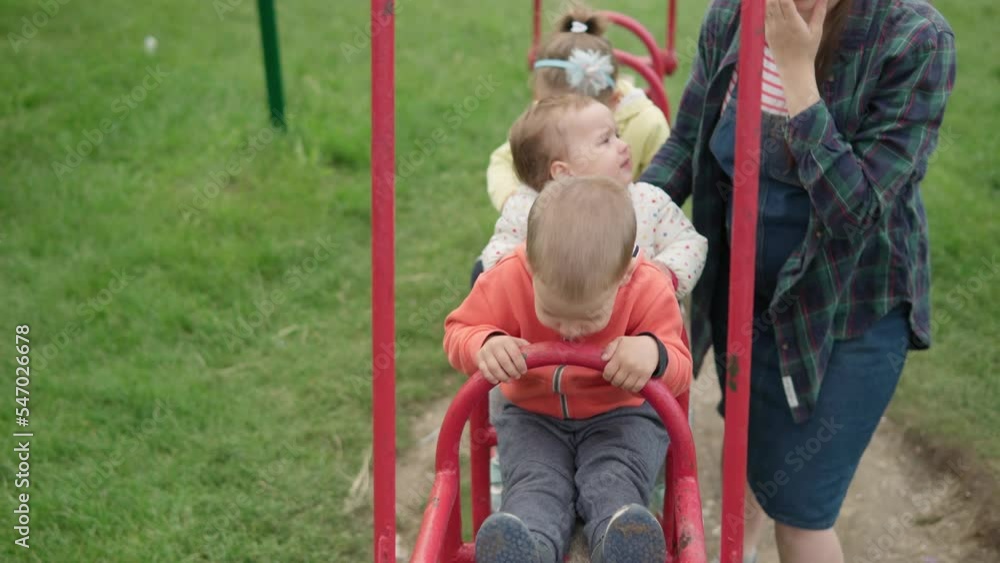 Cute pretty Preschool children with young mom frolic in swing train on playground. Little baby laughing have fun, swinging on seesaw board playing. Concept of happy childhood, positive emotions, POV Cute pretty Preschool children with young mom frolic in swing train on playground. Little baby laughing have fun, swinging on seesaw board playing. Concept of happy childhood, positive emotions, POV