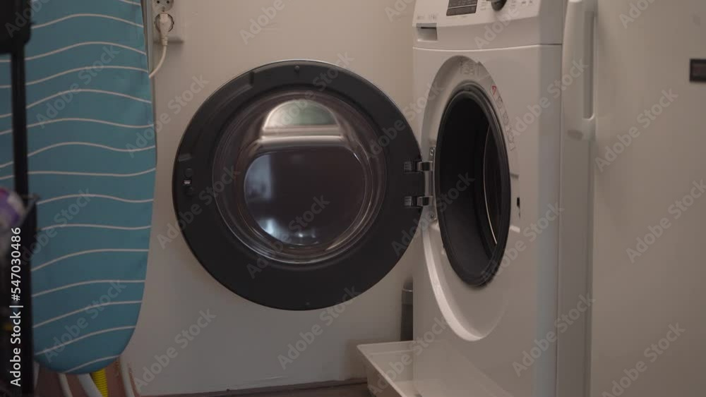 Young man picks up laundry basket from front load washing machine Young man picks up laundry basket from front load washing machine
