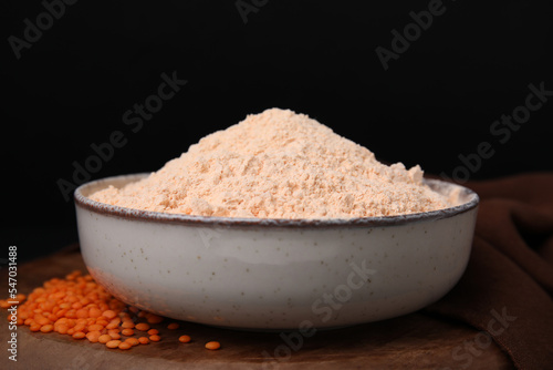 Bowl of lentil flour and seeds on wooden table against black background