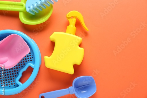 Bottle of suntan cream and children's beach toys on orange background, flat lay. Space for text