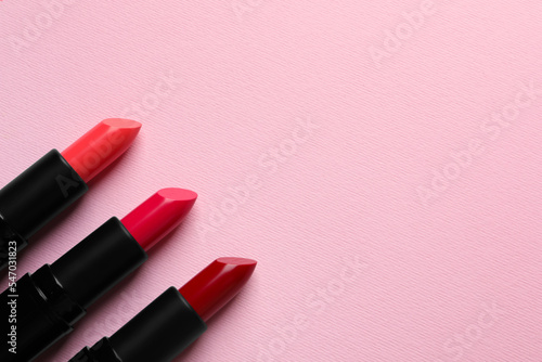 Many bright lipsticks on pink background, flat lay. Space for text