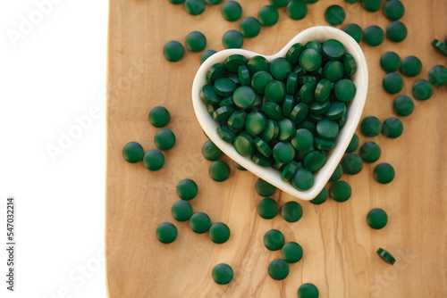 Spirulina tablets in cup in the shape of a heart on a wooden board on a white background.Vitamins and dietary supplements.Super food