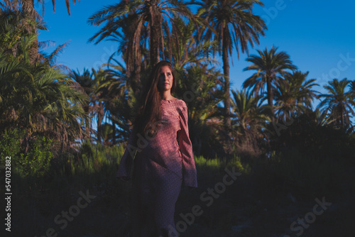 young pregnant woman relaxes in the golden light of sunset in a green natural place of plants and palm trees