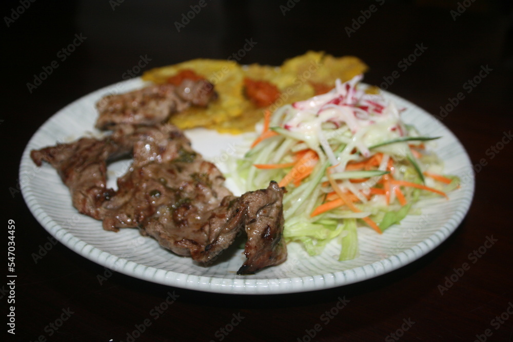 Roast beef with patacon and salad on dark wooden background