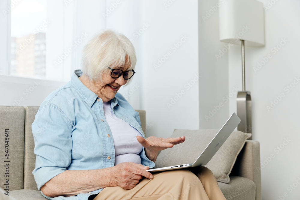 a joyful, funny old lady is sitting on a cozy sofa in a bright room and holding a laptop on her lap, working remotely despite her age a joyful, funny old lady is sitting on a cozy sofa in a bright room and holding a laptop on her lap, working remotely despite her age