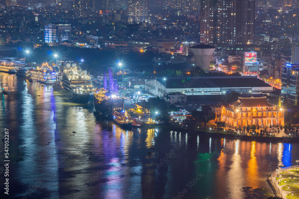 Classic night skyline under full lights of Ho Chi Minh City with Saigon river and large tourist boat. Travel and landscape concept.