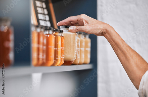 Honey, product and retail with hands of woman for natural, supermarket and grocery shopping shelf. Food, health and sustainability with organic store employee for small business, sale and choice photo