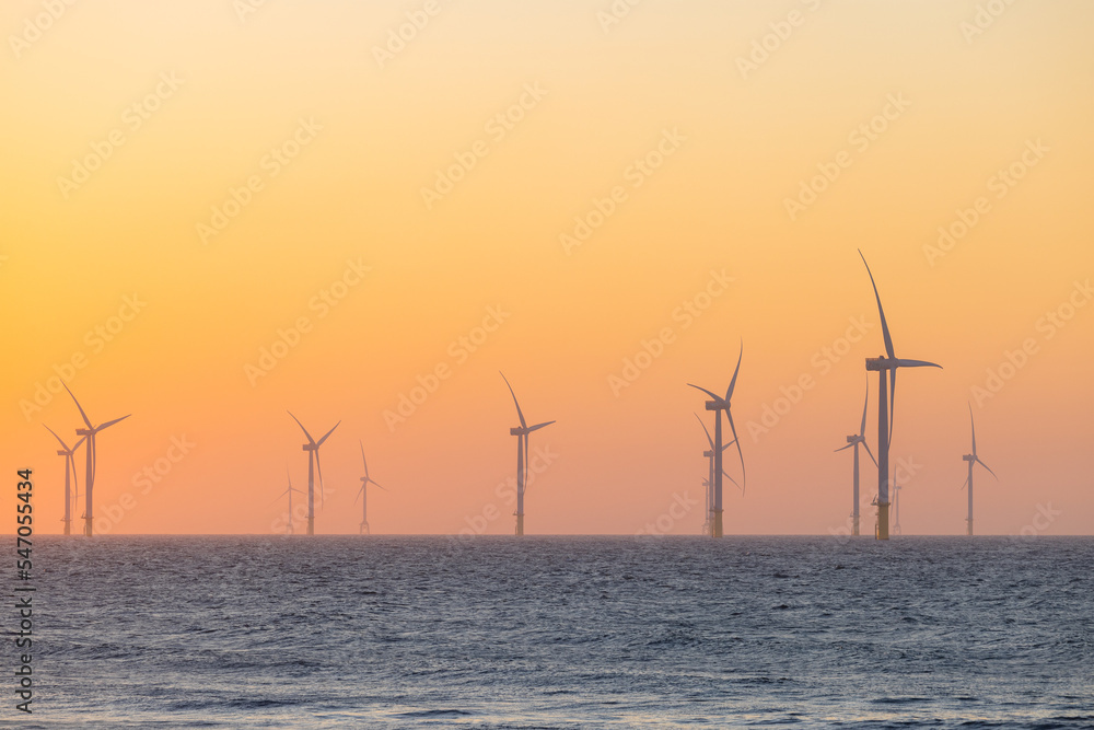 Large wind turbines producing plant on the sea under sunset