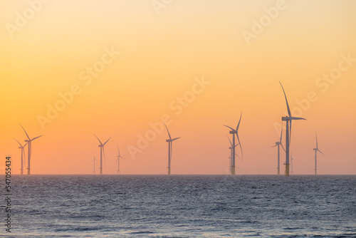 Large wind turbines producing plant on the sea under sunset