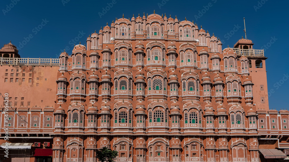 The ancient Palace of the Winds- Hawa Mahal against the blue sky. The five-storey red sandstone building in the form of the crown of Krishna. There are many windows with openwork grilles on the facade
