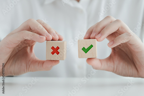 Hand holding green correct check mark and red wrong or cross icon on wooden block for true or false changing mindset or way of adapting to change leader, transform quiz answer, yes or no poll concept.