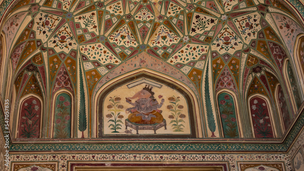 A fragment of an ancient painting on the ceiling. The God Ganesha is depicted on a couch surrounded by geometric and floral designs. India. Jaipur Amber Fort