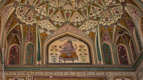 A fragment of an ancient painting on the ceiling. The God Ganesha is depicted on a couch surrounded by geometric and floral designs. India. Jaipur Amber Fort