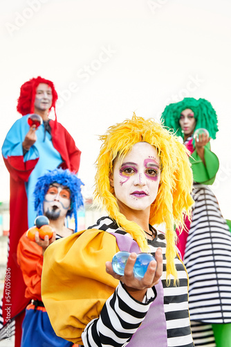 Male and female clowns in colorful costumes and wigs, looking at the camera holding crystal balls in their hands.