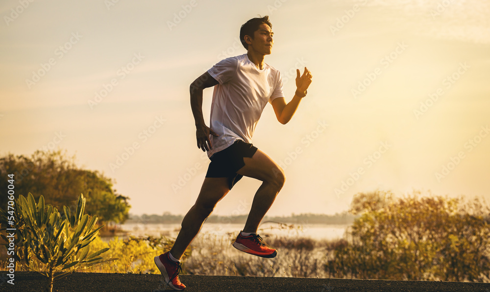 Silhouette of young man running sprinting on road. Fit runner fitness runner during outdoor workout with sunset background.