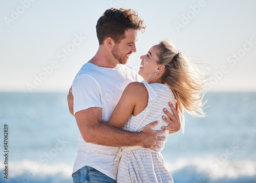 Love, beach hug and couple smile together at the ocean for peace, relax in nature and romance vacation happiness. Happy man, laughing woman and relationship bliss on a travel holiday by sea